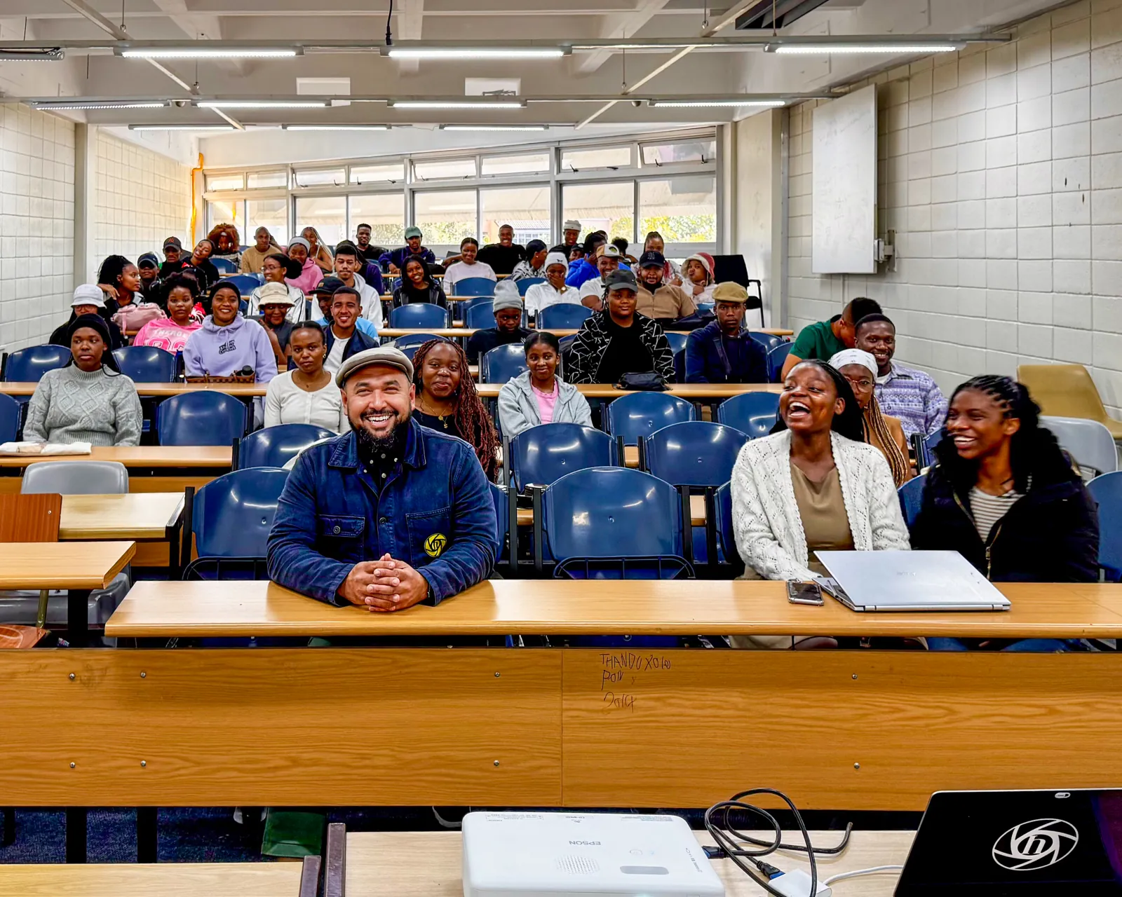 Khaalid sitting among smiling students in a university lecture hall