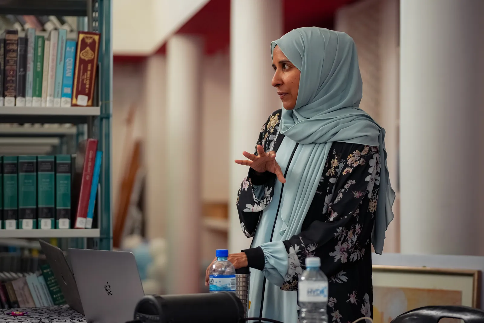 A facilitator speaking to attendees beside a library bookshelf